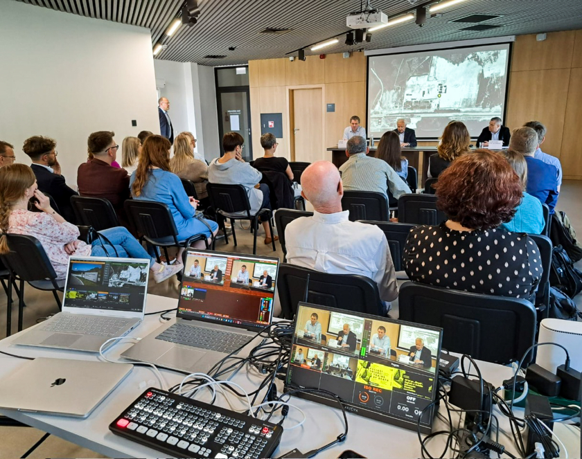 Grupa osób w sali edukacyjnej słuchających debaty, na pierwszym planie laptopy oraz sprzęt elektroniczny służący do transmisji.