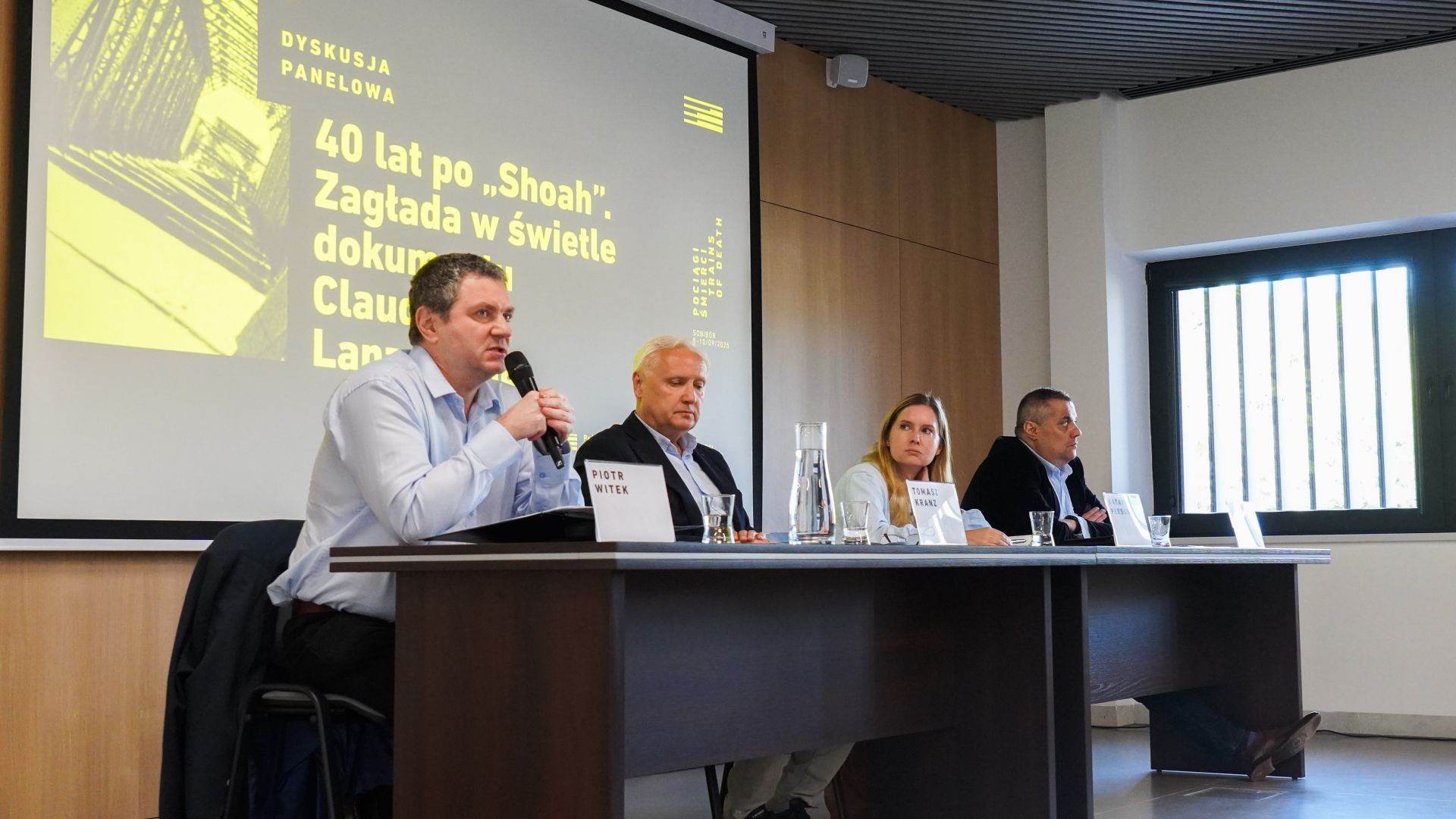 Cztery osoby, trzech mężczyzn i kobieta siedzą przy stole, w tle na ekranie grafika: dyskusja panelowa, 40 lat po Shoah Zagłada w świetle dokumentu (reszta nieczytelna) 