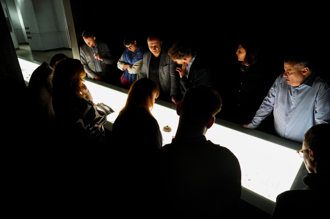 Grupa osób nad podświetloną gablotą w ciemnej sali 