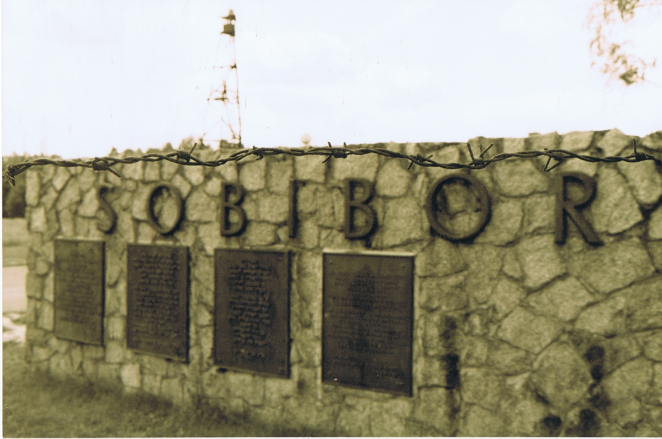 A stone wall with metal letters forming the word ‘SOBIBOR’, with four metal plaques featuring raised engravings below.