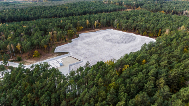 Aerial photograph, huge graveyard covered with white stones and enclosed with a concrete wall is visible among the vast forest.