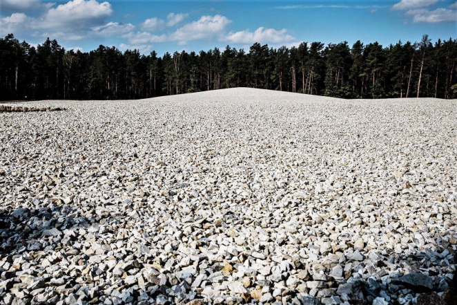 Mound covered with white aggregate stones, many pine trees are visible in the background.