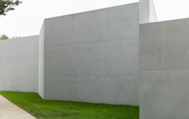 Huge, grey wall erected in the vicinity of green area.