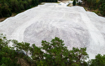 Aerial view of a mound covered in white gravel, it is surrounded with trees.