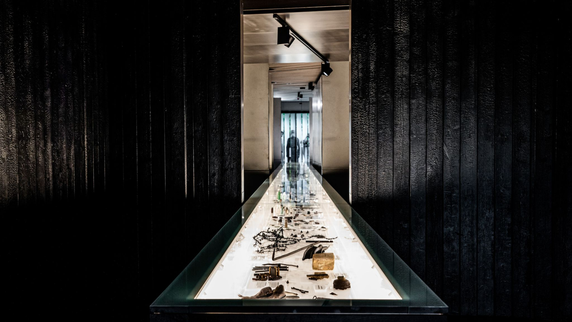 A long, white, bright, glass-fronted display case containing numerous objects, positioned between two black wooden walls.