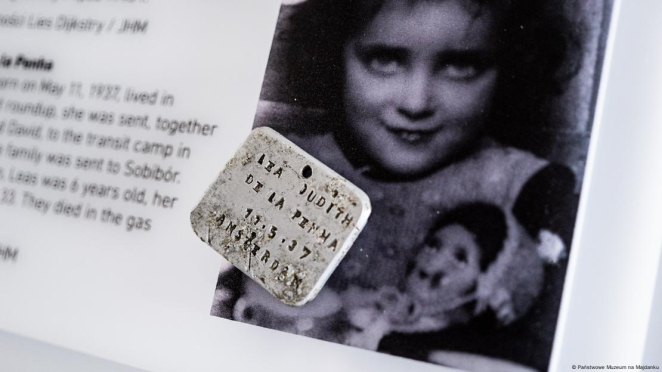 A rectangular metal plaque with an engraving reading: Lea Judith De La Penha, 11 May 1937, Amsterdam; in the background, a photograph of a little girl with brown, curly hair holding a doll.