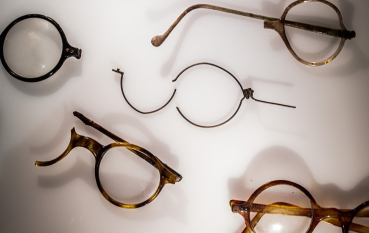 Several pairs of round-framed glasses in a lighted display case, some with tortoiseshell frames, and one pair with black frames.