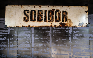 Old, rusty, white board with the name Sobibor painted in black.