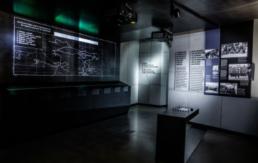 A view of the exhibition, illuminated display panels, an interactive map, and panels featuring historical information and photographs.