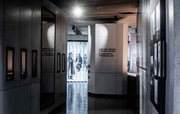 A view of the exhibition: on the left, five glass display cases built into the wall; on the right, exhibition panels featuring historical information and displays; in the centre, an inscription on the wall: ‘Crime scene – Memorial site’.