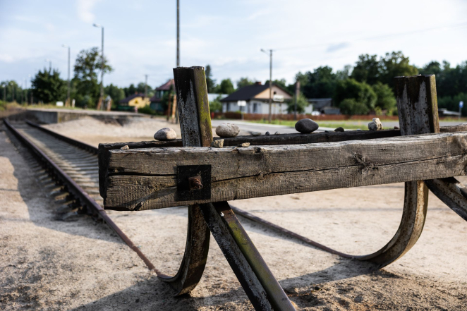 Drewniany kozioł oporowy, na nim rząd kamieni, na drugim planie tory kolejowe.