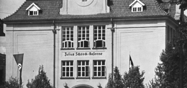 Czarno-białe zdjęcie budynku o charakterystycznym wykuszu; okno w eliptycznej formie zwieńczone półokrągłym daszkiem, wsparte na dwóch cokołach. 