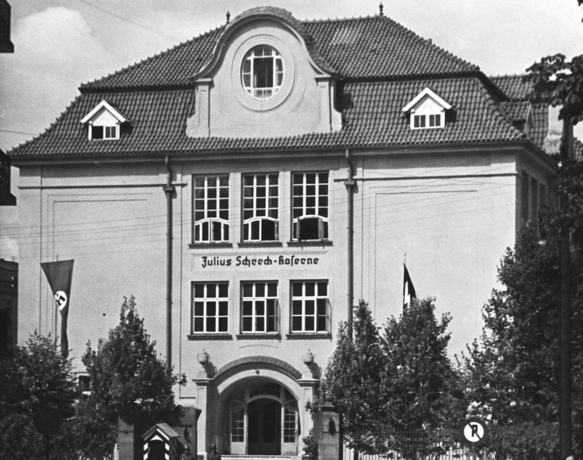 Czarno-białe zdjęcie budynku o charakterystycznym wykuszu; okno w eliptycznej formie zwieńczone półokrągłym daszkiem, wsparte na dwóch cokołach.