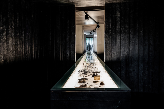 Mlecznobiała, podświetlana gablota z przedmiotami w czarnym pomieszczeniu. 