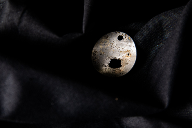 Metalowa okrągła plakietka, porysowana z uszkodzeniami w kształcie dziur, tło: czarne, aksamitne. 