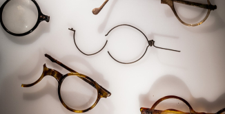 Kilka par połamanych okularów w podświetlanej białej gablocie.