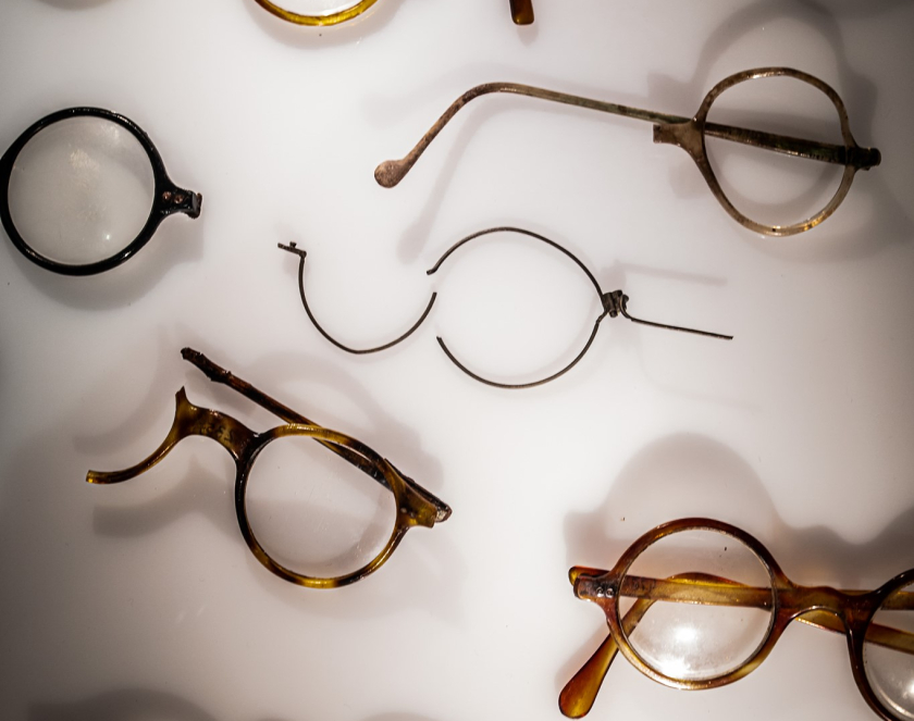 Kilka par połamanych okularów w podświetlanej białej gablocie. 