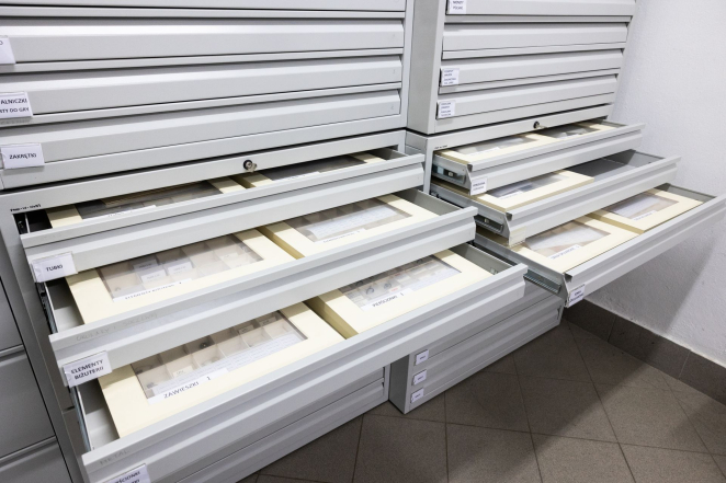 Metalowa komoda z licznymi metalowymi szufladami, w szufladach bezkwasowe pudełka z drobnymi muzealiami. 