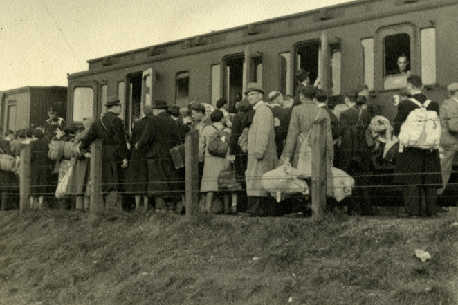 A group of elegantly dressed people with suitcases and backpacks in front of a train carriage