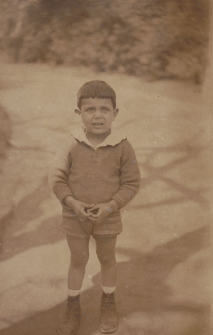 Zdjęcie sepia, kilkuletni chłopiec ubrany w krótkie spodenki i bluzkę z białym kołnierzykiem. 