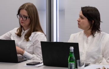 Dwie kobiety w białych koszulach siedzą przy laptopach 