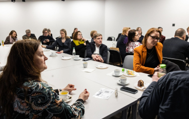 Grupa osób siedząca przy stolikach. 