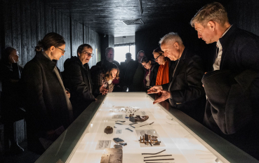 Grupa osób nad podświetloną gablotą z przedmiotami.