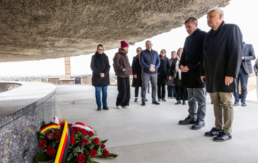 Dwóch mężczyzn, za nimi grupa osób składa hołd pod kopułą Mauzoleum, przed nimi wiązanka z polską i niemiecką flagą. 